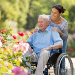 Caregiver with senior client in wheelchair looking at flowers