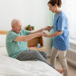 Caregiver assisting senior man getting out of bed